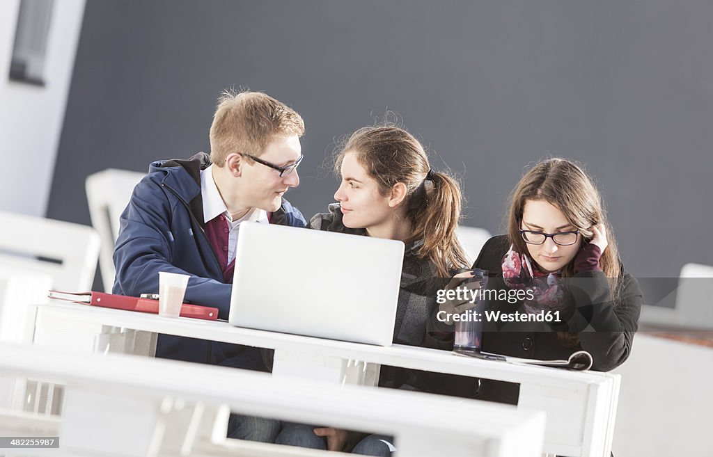 Three students using laptop outdoors
