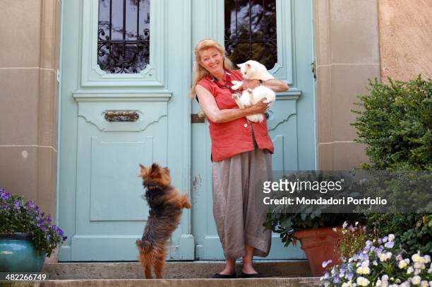 Margherita Agnelli de Pahlen posing on the threshold of her villa at Lake Geneva, with a big, white cat in her arms, surrounded by vases of flowers...
