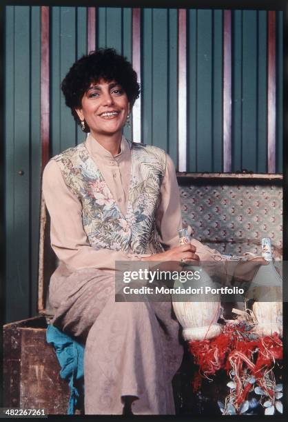 Italian singer Mia Martini smiling and holding two small flasks of wine. 1990s