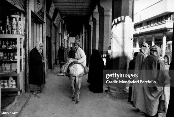 An Iraqi boy riding a donkey under the porches of Al Rasheed street in front of a shop. Baghdad, December 1956