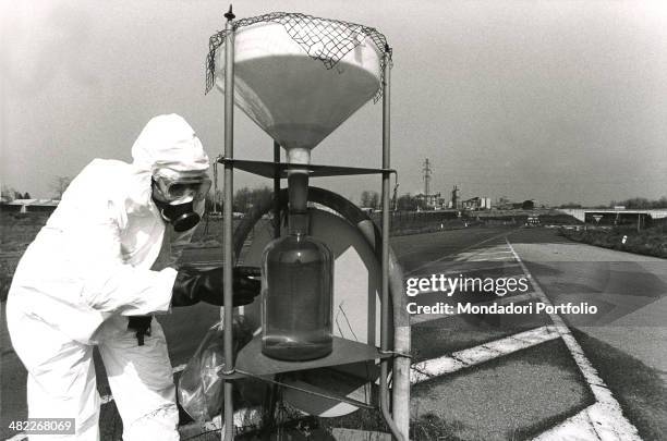 Qualified worker wearing white coverall and a gas mask appointed to free from pollution the A area in Seveso analyzes a sample survey of liquid: on...