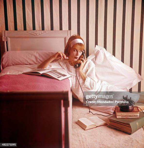 Girl in pyjamas speaking over the phone in a pink bedroom. 1960s