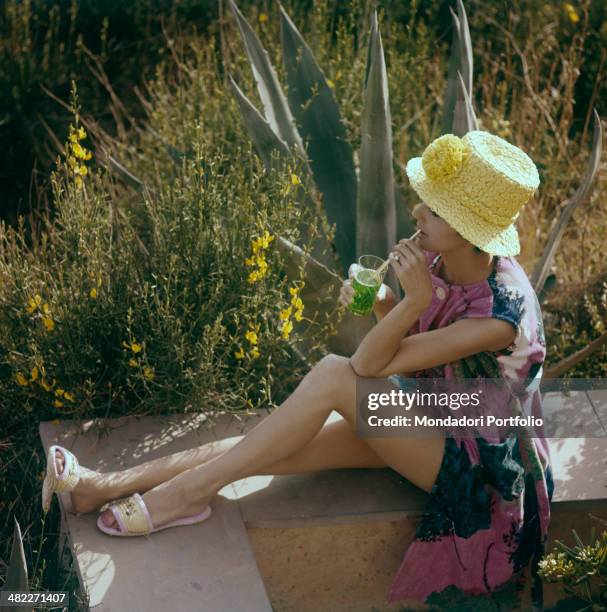 Young woman drinking using a straw and looking at the panorama. Italy, June 1962