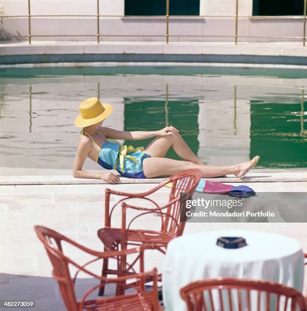 Girl in swimsuit and straw hat sunbathing by the swimming pool. 1960s