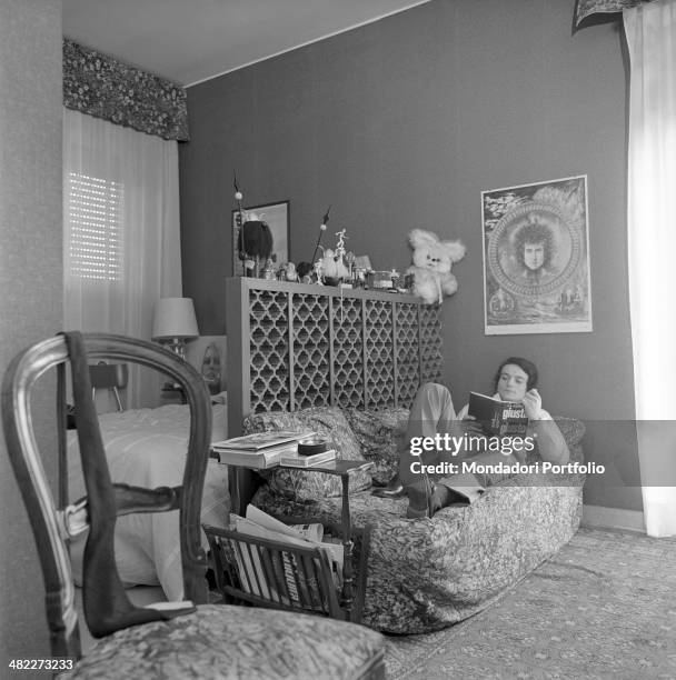 Italian singer Massimo Ranieri reading the book La parola giusta al momento giusto lying on the sofa in front of a poster depicting Bob Dylan at...