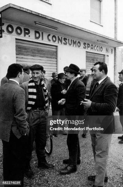 Some men chatting in front of the Coop di Consumo Spaccio n.8 in the most communist village of Italy, Taglio Corelli. Taglio Corelli, October 1965