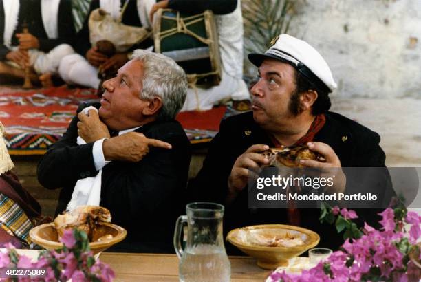 Italian actor Paolo Villaggio pointing at Italian actor Lino Banfi holding a chicken in the film Com'è dura l'avventura. 1987