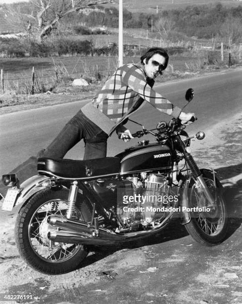 Italian actor and singer Fabio Testi getting on a Honda motorcycle. Rome, 1974