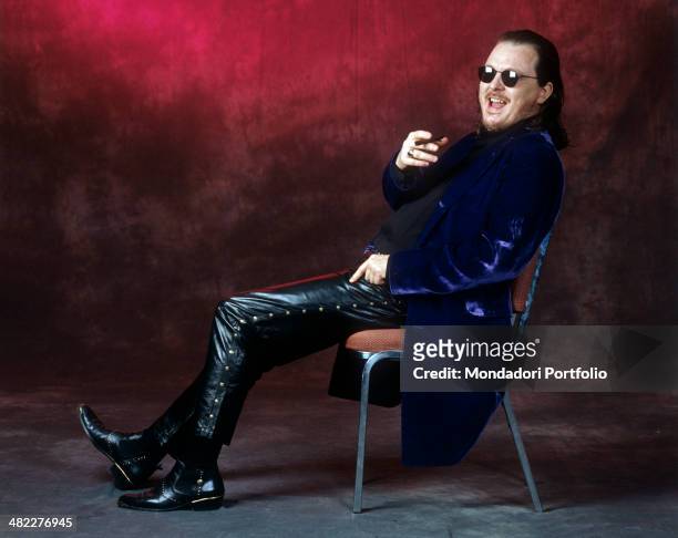 Italian singer-songwriter and musician Zucchero sitting on a chair in leather pants with a cigar in his mouth. 1996