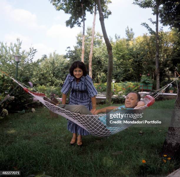 Italian singer and actor Claudio Villa posing lying on a hammock beside his Italian wife Patrizia Baldi. 1975