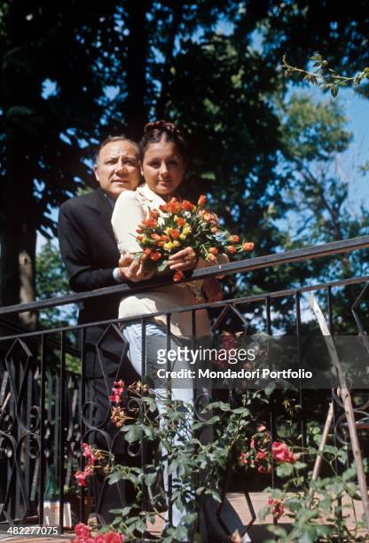 Italian singer and actor Claudio Villa posing his Italian wife Patrizia Baldi holding a bunch of flowers. 1975