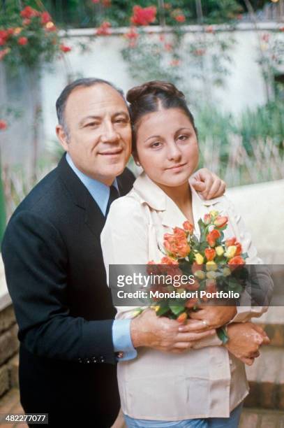 Italian singer and actor Claudio Villa hugging his Italian wife Patrizia Baldi holding a bunch of flowers. 1975