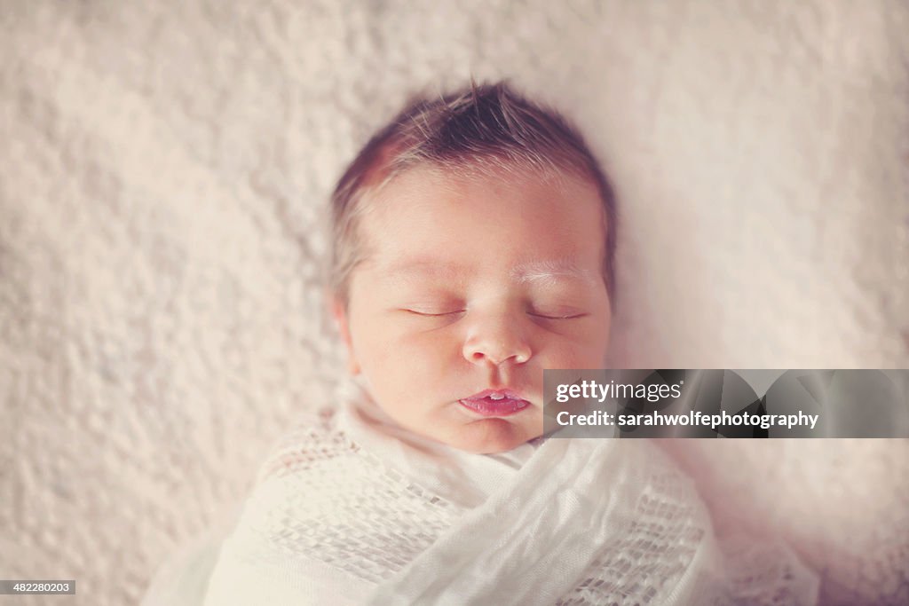 Sleeping baby swaddled on white blanket