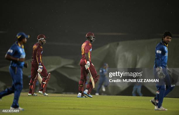 West Indies cricket captain Darren Sammy walks off the field as Bangladesh groundstaff pull the covers towards the wicket while heavy rain falls...