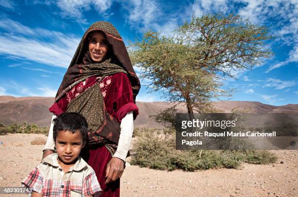 Portrait of Berber woman in traditional clothing next to an acacia tree in the hammada desert near Tata.