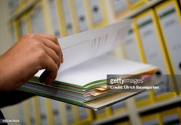 Symbol photo bureaucracy - hands holding a file folder in front of a file shelving.