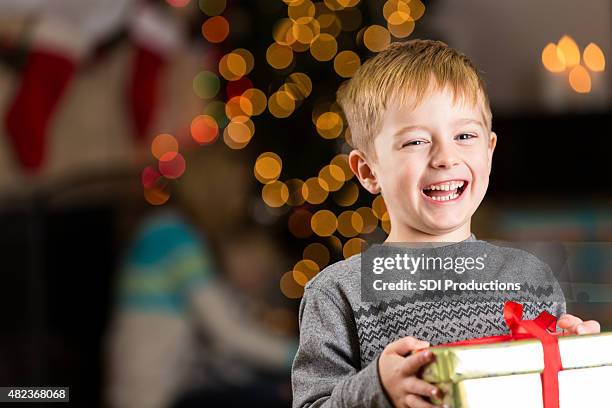 excited young boy holding present on christmas day - giving tree stock pictures, royalty-free photos & images