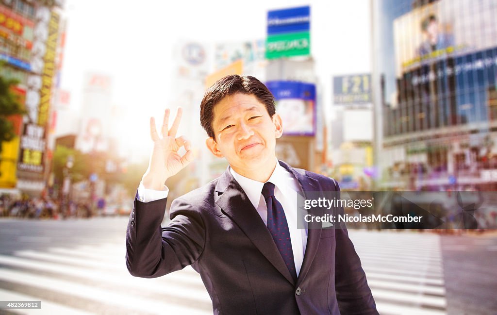 Proud Japanese businessman making ok sign Shibuya crossing Tokyo Japan