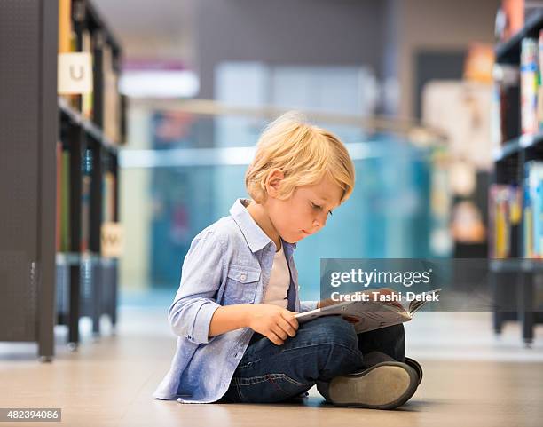 adorable little boy sitting in library - kid reading stock pictures, royalty-free photos & images