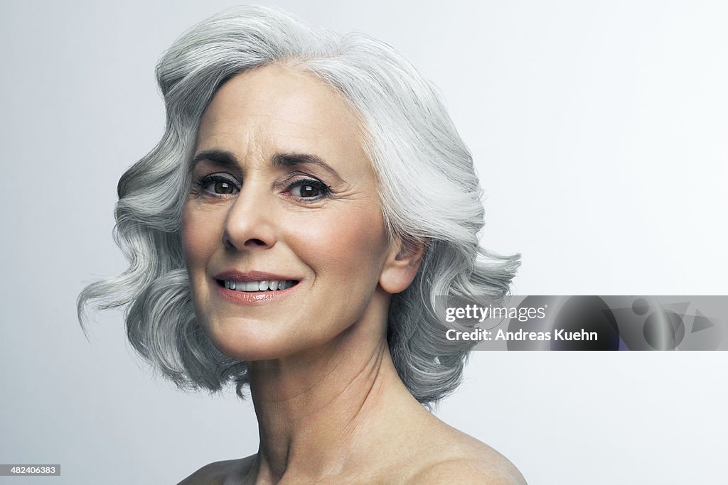 Woman with wavy, grey hair smiling, portrait.