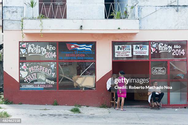 Cuban everyday scene: Storefront at New Years', workers sitting outside a government run cafeteria, getting paid doing nothing. The building is...