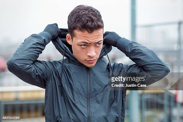 young sporty man puts his hood on in the city - uomo incappucciato foto e immagini stock