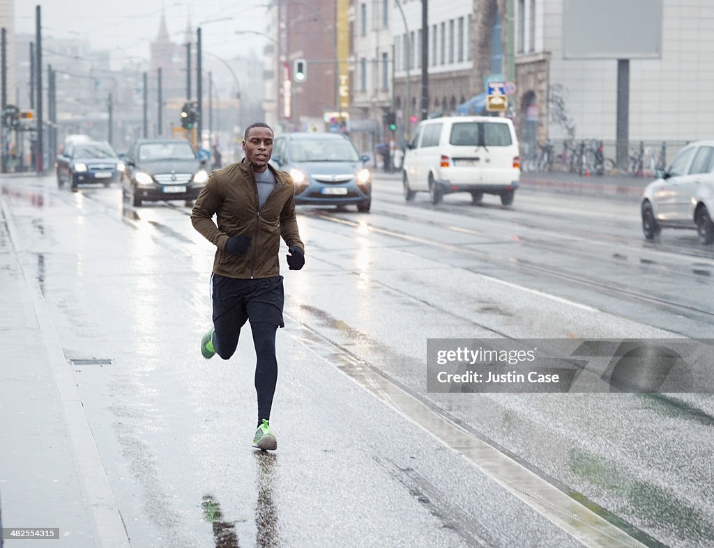 Sporty man jogging through rainy city scape