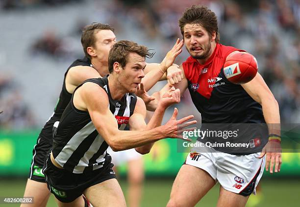Matt Scharenberg of the Magpies handballs whilst being tackled by Jesse Hogan of the Demons during the round 18 AFL match between the Collingwood...