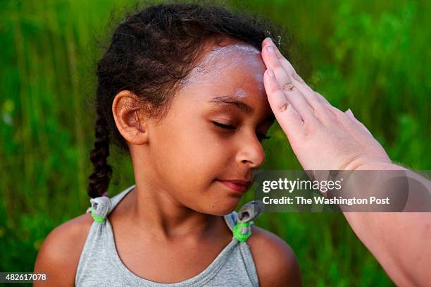 Laura Halapin of Virginia Beach, rubs sunscreen on her daughter Christine's face before the 88th Annual Pony Swim across the Assateague Channel on...