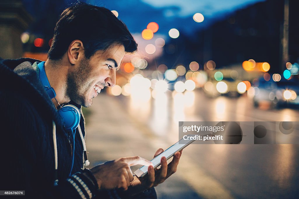 Man with digital tablet and headphones, outdoors at night traffic