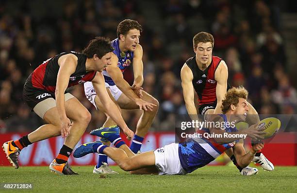 Mitch Wallis of the Bulldogs handballs whilst being tackled by Zach Merrett of the Bombers during the round 18 AFL match between the Essendon Bombers...