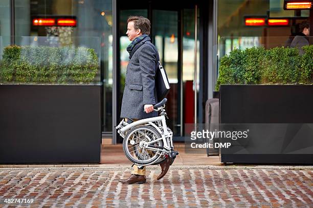 middle aged businessman carrying his folding bicycle - foldable stockfoto's en -beelden
