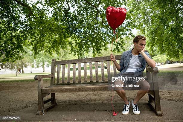 heartbroken man at the park holding a heart shaped balloon - broken heart stock pictures, royalty-free photos & images