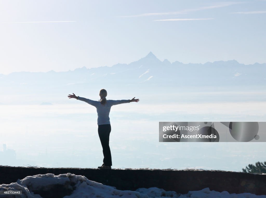 Woman standing on rock bluff with arms out