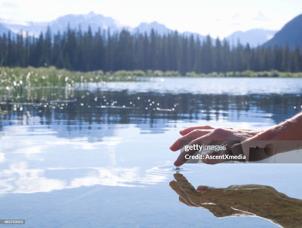 Person's finger touching surface of mountain lake