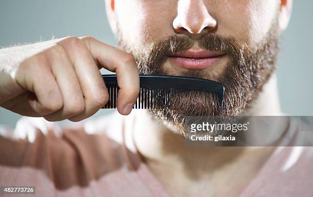 unrecognizable man combing his beard - haircare stockfoto's en -beelden