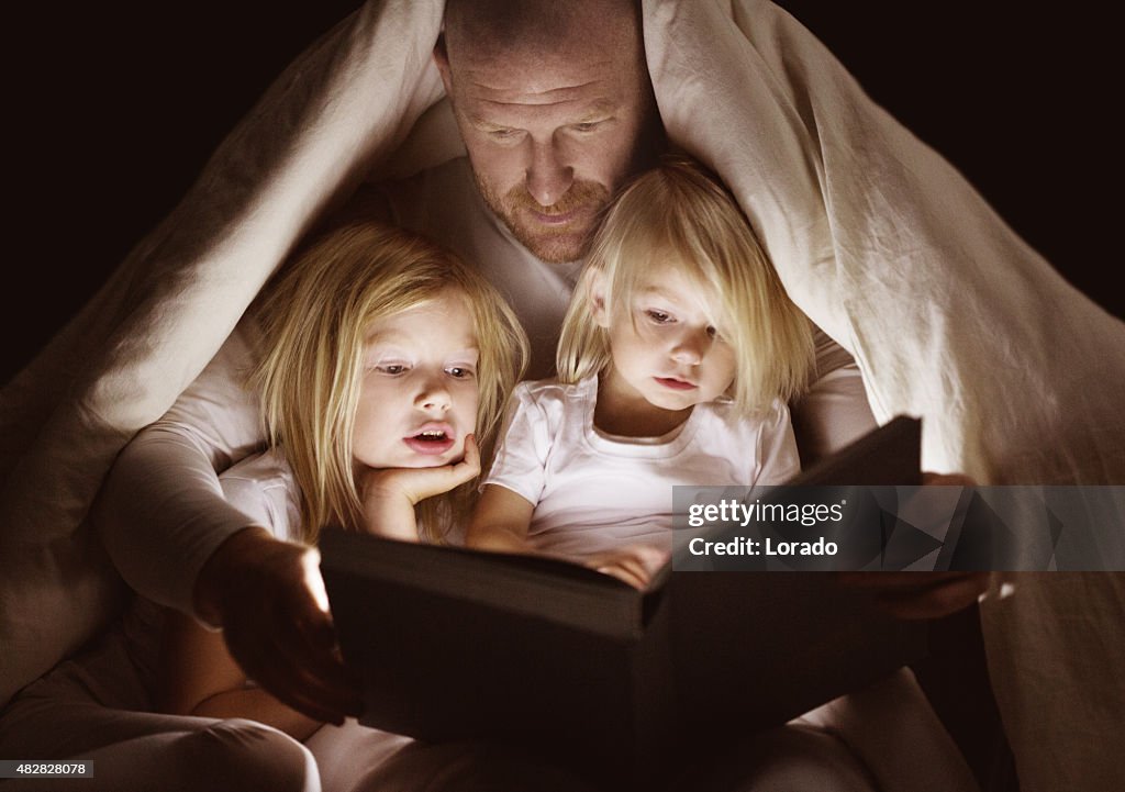 Father and daughters reading book at bedtime