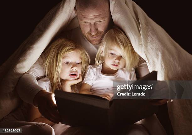 father and daughters reading book at bedtime - disney stock pictures, royalty-free photos & images