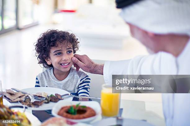 middle eastern grandfather talking with his grandson while eating - united arab emirates food stock pictures, royalty-free photos & images