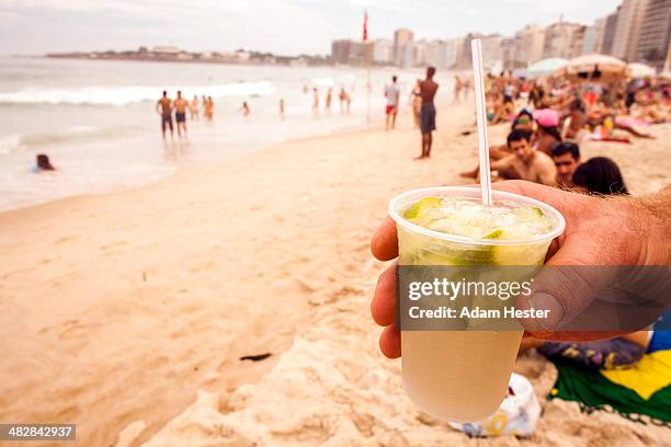 a man holding a caipirinha on ipanema beach. - caipirinha foto e immagini stock