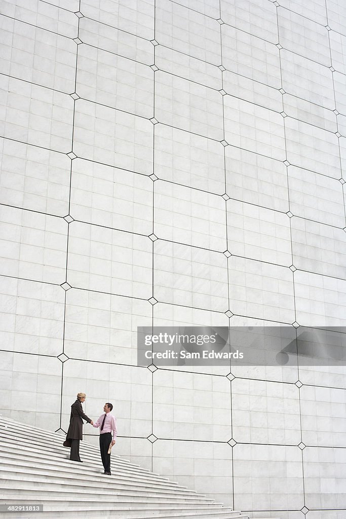 Two businesspeople outdoors on staircase shaking hands