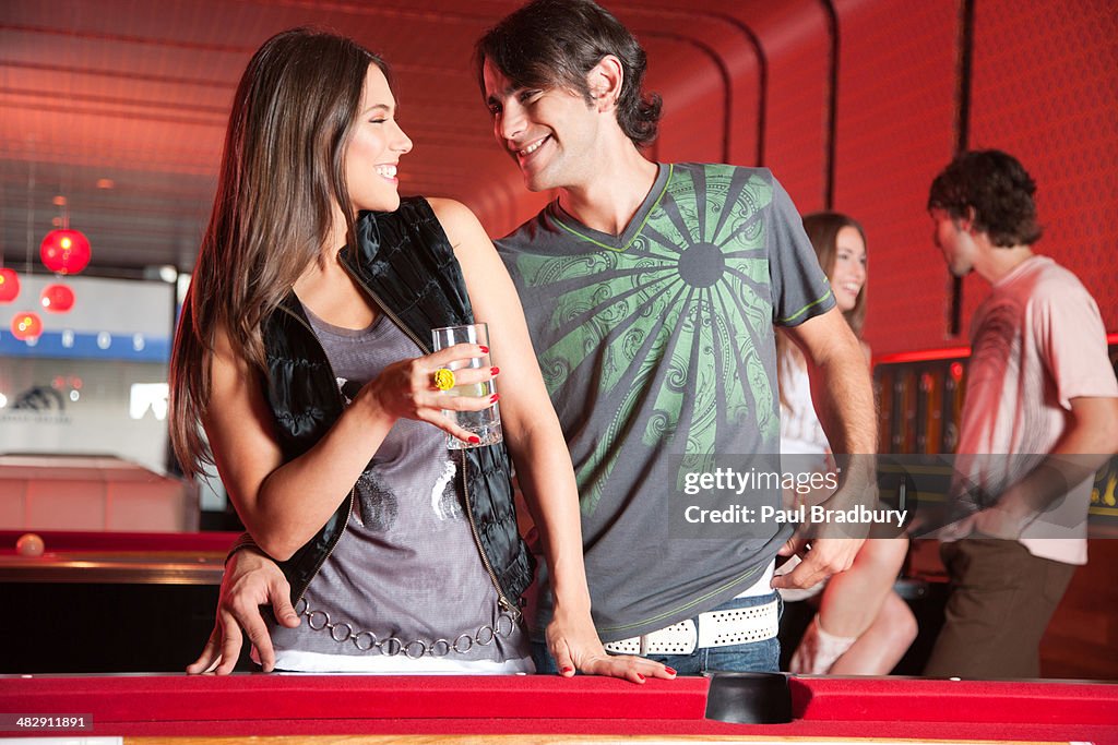 Couple with beverages standing by pool table smiling