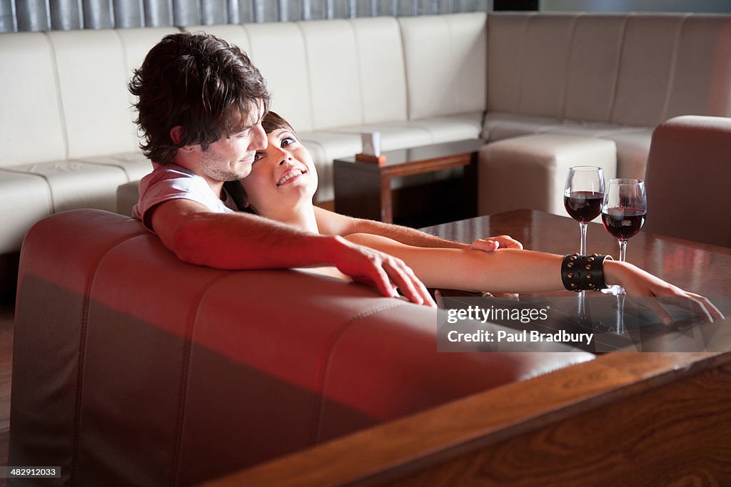 Couple relaxing on living room sofa with red wine on table