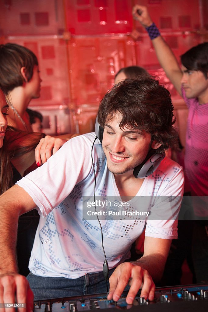 Disc jockey in nightclub with people dancing around him smiling