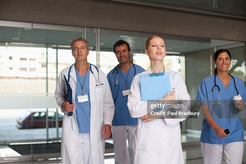 Four hospital workers walking in corridor holding clipboards and smiling