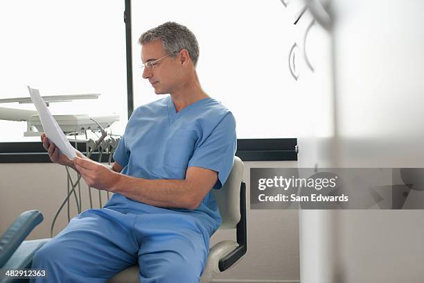 dentist standing in examination room looking at charts - a male dentist stock pictures, royalty-free photos & images