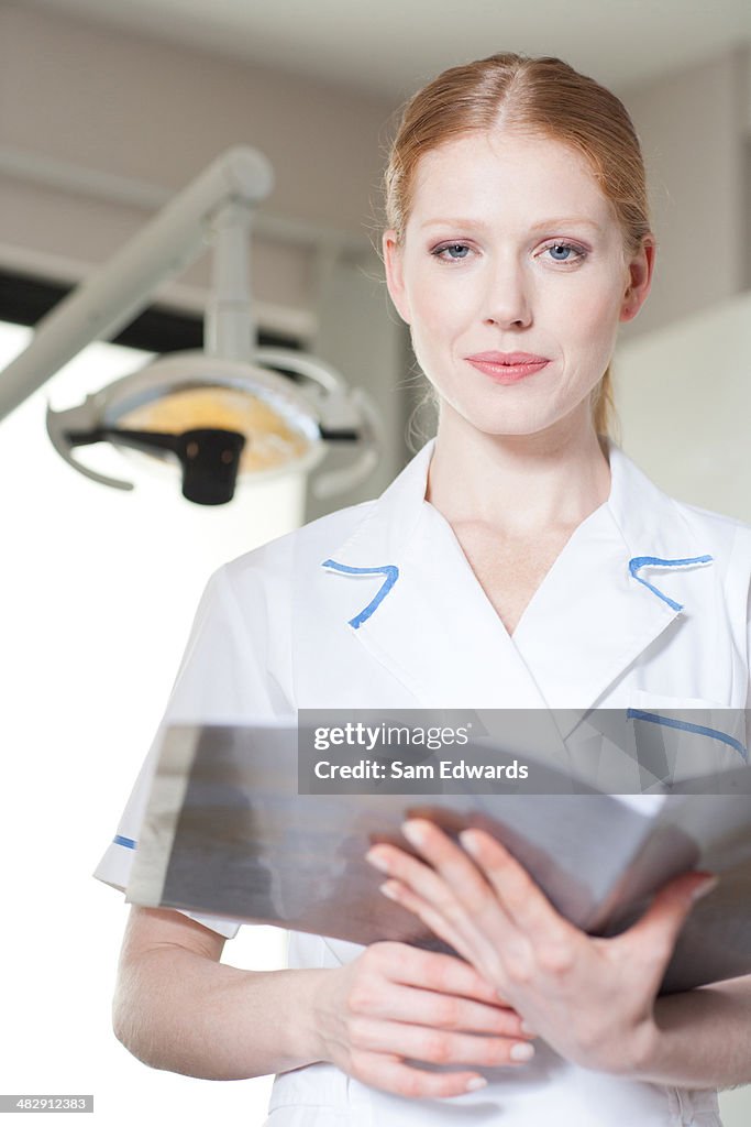 Dental assistant in examination room holding charts and smiling