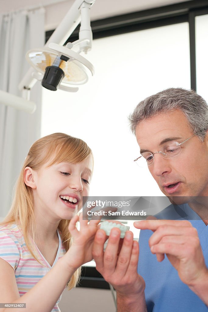 Dentist in examination room showing smiling young patient mold of teeth