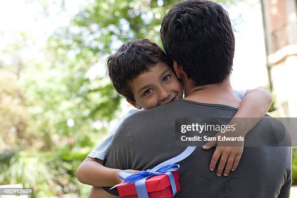 mann, umarmen lächelnde junge holding geschenk im freien - child giving gift stock-fotos und bilder