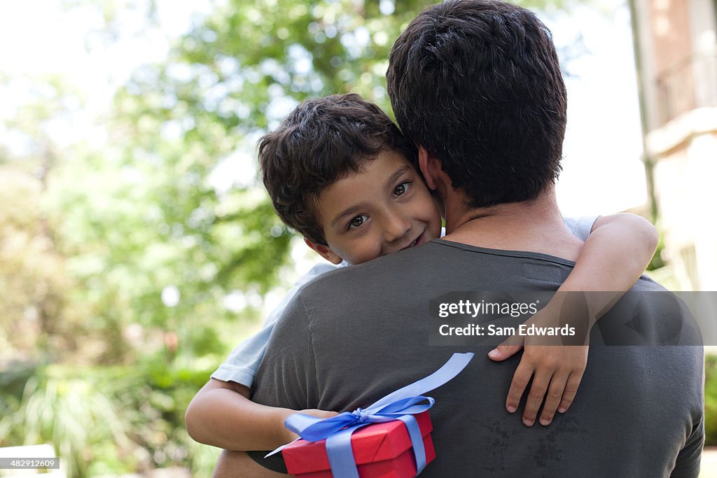 Man hugging smiling young boy holding gift outdoors